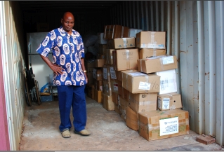 Mr. J. J. Mayovu standing by the 65 boxes of books stored in a large metal container.